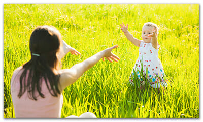Child with outstretched arms running in field to mother